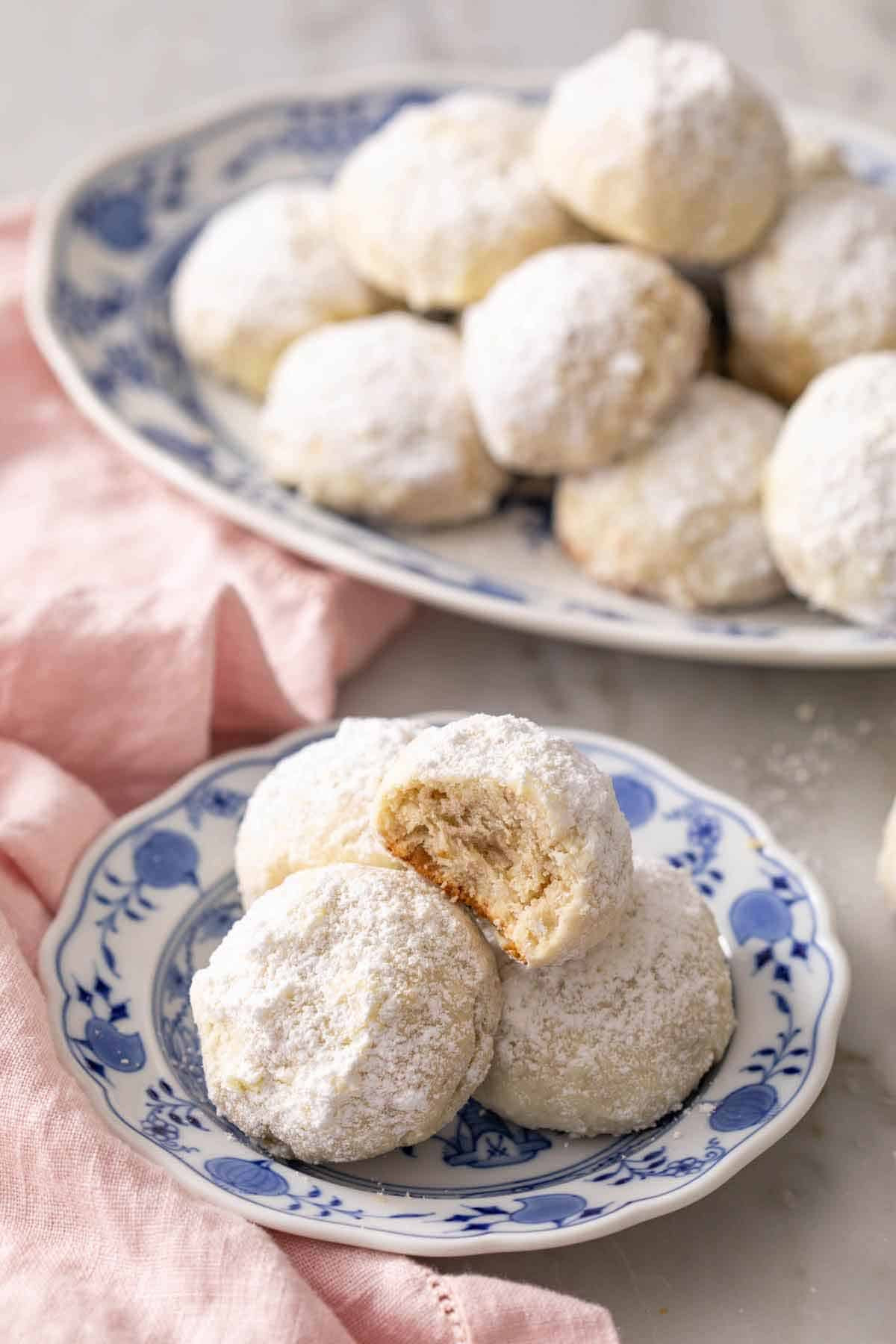 A plate of Mexican wedding cookies, with one cookie on top having a bite taken out to show the texture.
