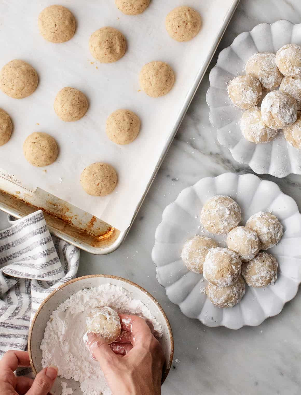 Hands dusting Mexican wedding cookies with powdered sugar