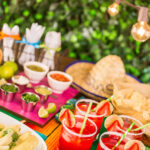 Buffet setup for a Mexican fiesta party, featuring serape tablecloths and clay pots.