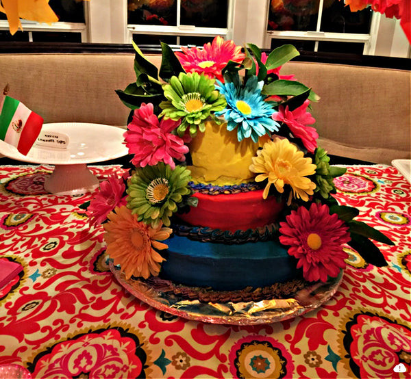 A colorful Mexican birthday cake decorated with artificial flowers, demonstrating a simple yet festive dessert idea.