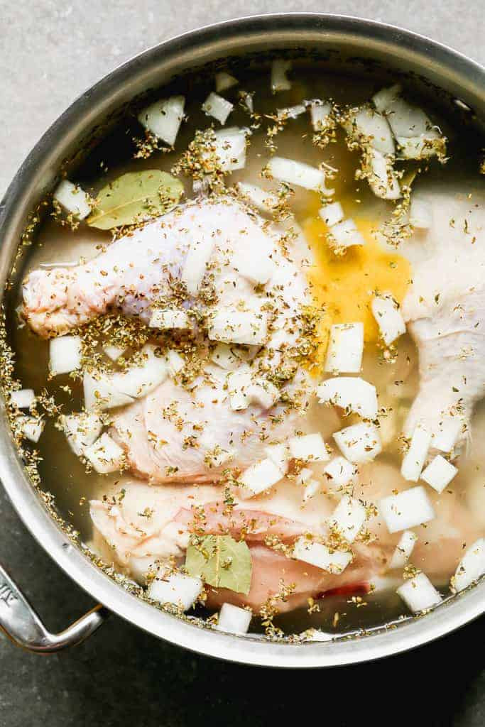 Chicken pieces simmering in a large pot with water, onions, and various spices, illustrating the first step in preparing chicken for mole.