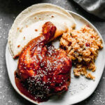 A plate with rich mole sauce generously poured over tender chicken, accompanied by a side of vibrant Mexican rice and soft corn tortillas.