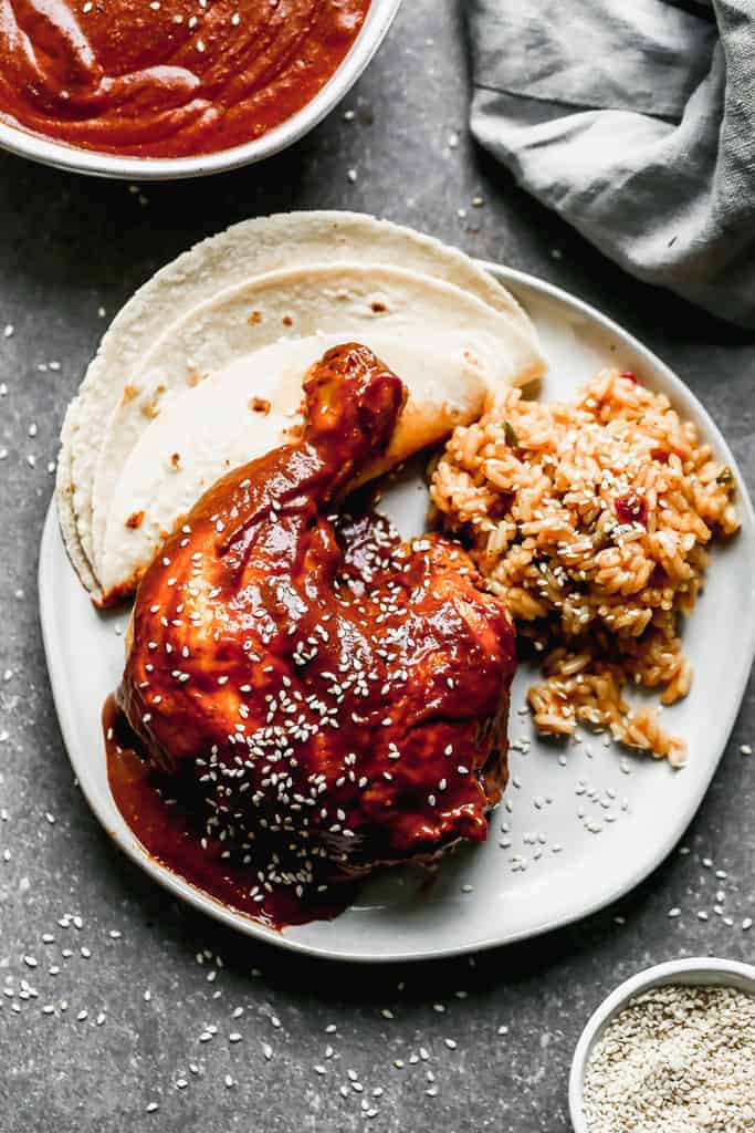 A plate with rich mole sauce generously poured over tender chicken, accompanied by a side of vibrant Mexican rice and soft corn tortillas.