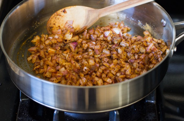 Close-up of spices being added to sautéed onions in a skillet, enhancing the base flavor of the Mexican Rice Casserole.