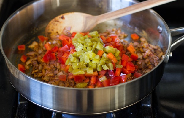 Adding diced bell pepper and green chilies to the skillet with onions and spices for a vibrant Mexican flavor base.