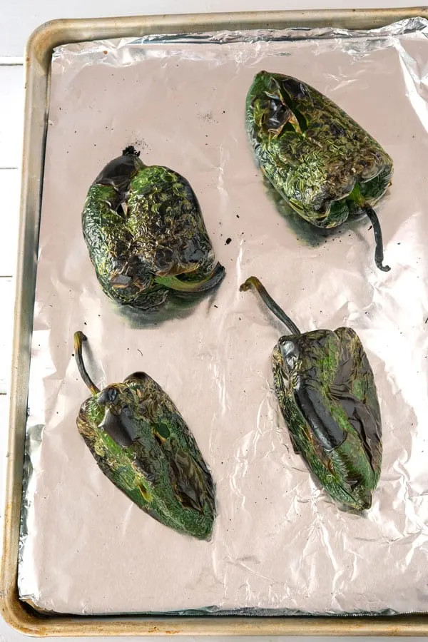 Close-up of four roasted poblano peppers showing the charred skin, emphasizing the result of the roasting process