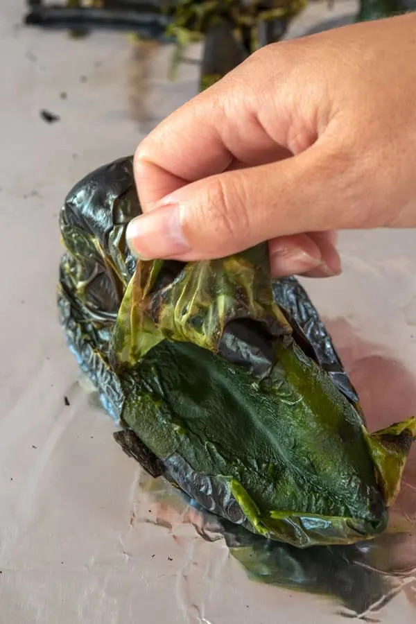 Hands peeling the skin off a roasted poblano pepper, showing the ease of peeling after steaming