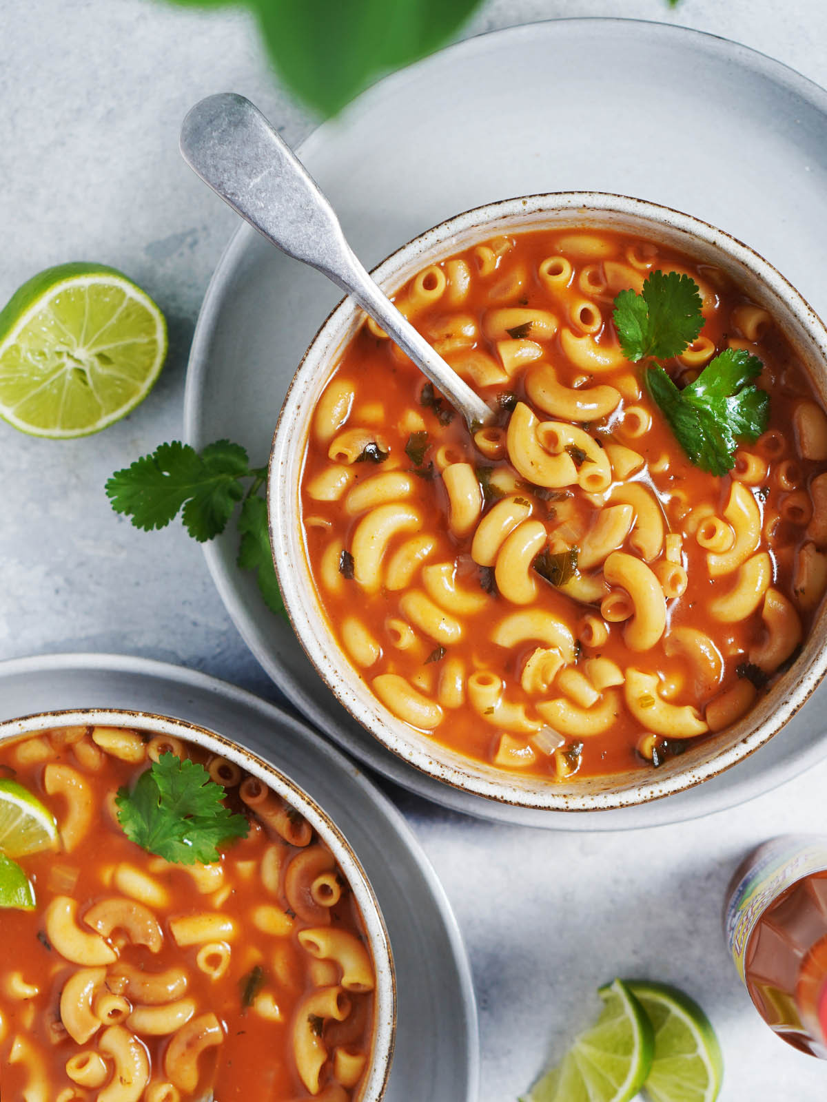 Two bowls of mexican sopa in a vibrant red broth, garnished with lime wedges.