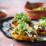 Three mexican sopes topped with chorizo and lettuce on a plate.