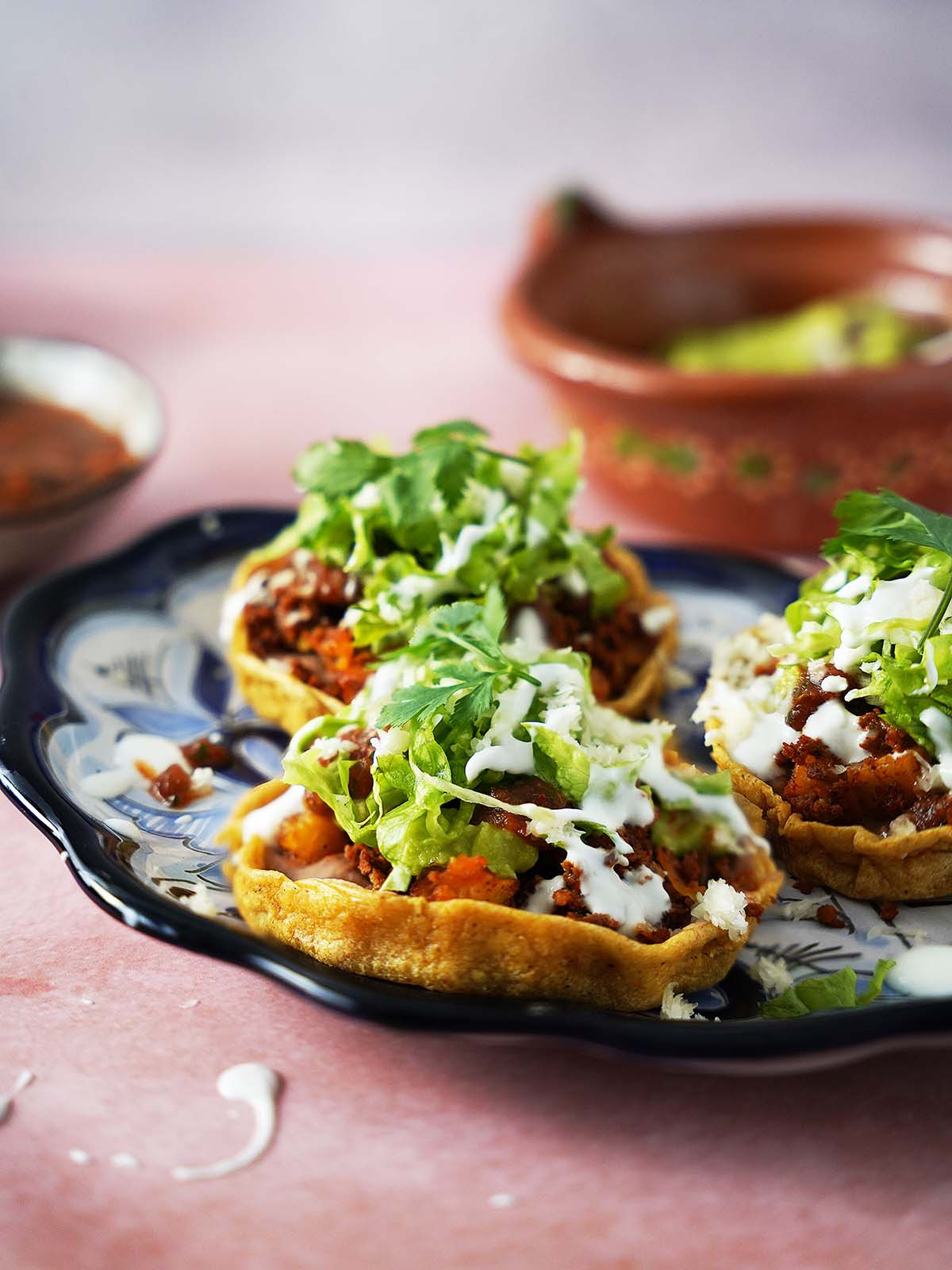 Three mexican sopes topped with chorizo and lettuce on a plate.