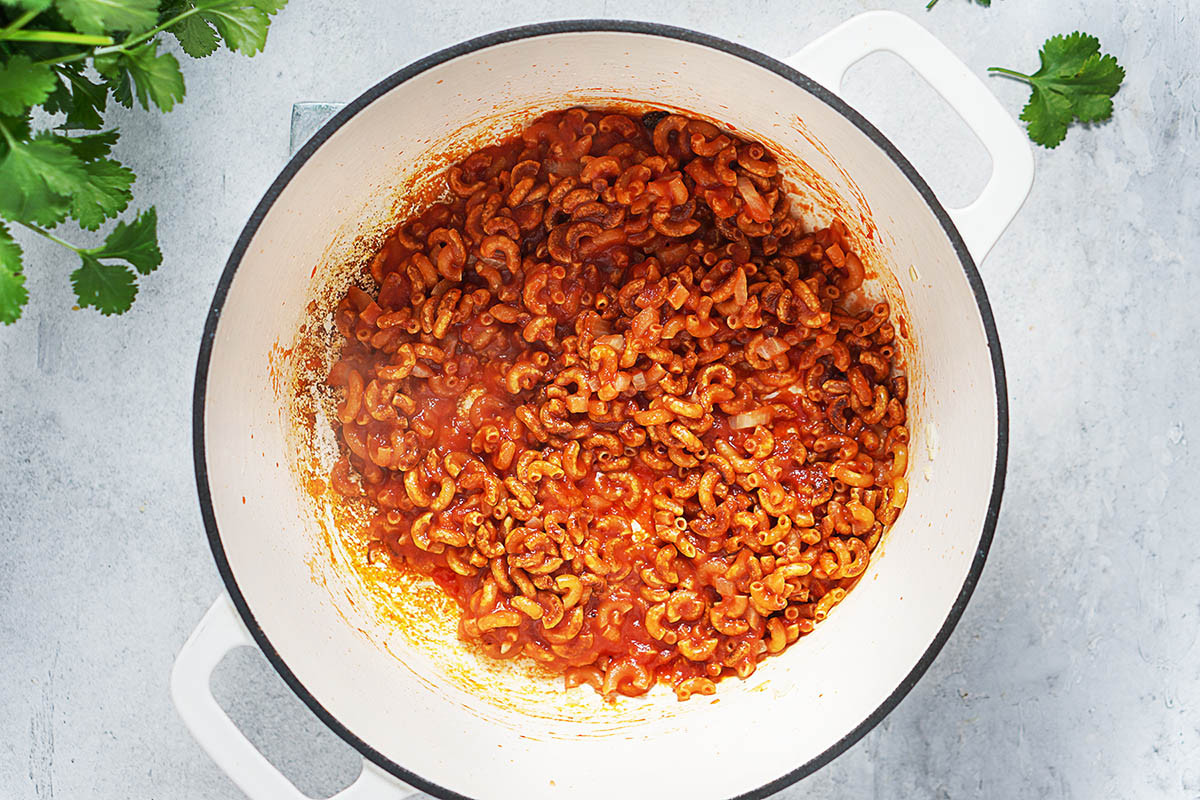 Adding tomato sauce to toasted pasta and onions for mexican sopa.