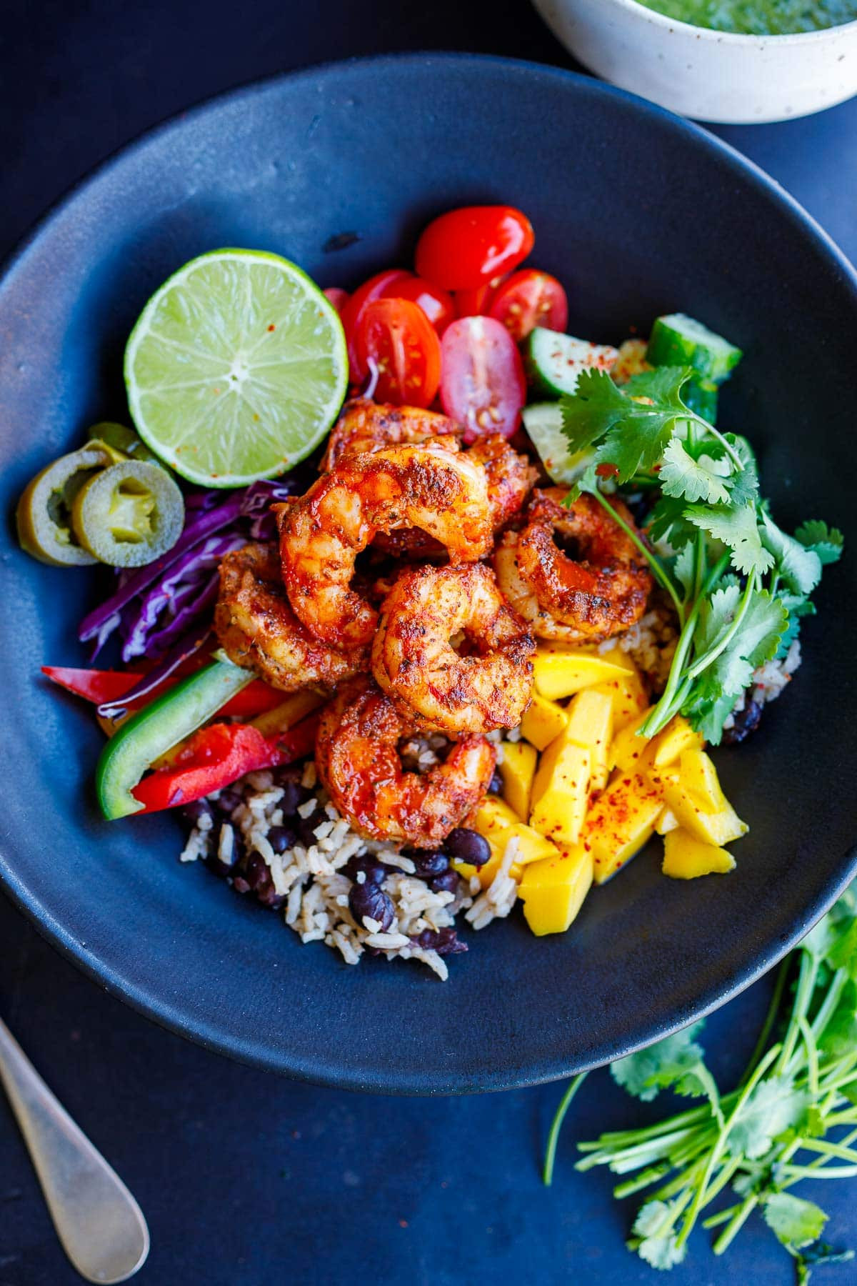 Spicy Mexican shrimp bowl filled with rice and beans, mango, cilantro, cucumber, tomato, lime, pickled jalapeno, cabbage, and bell peppers.