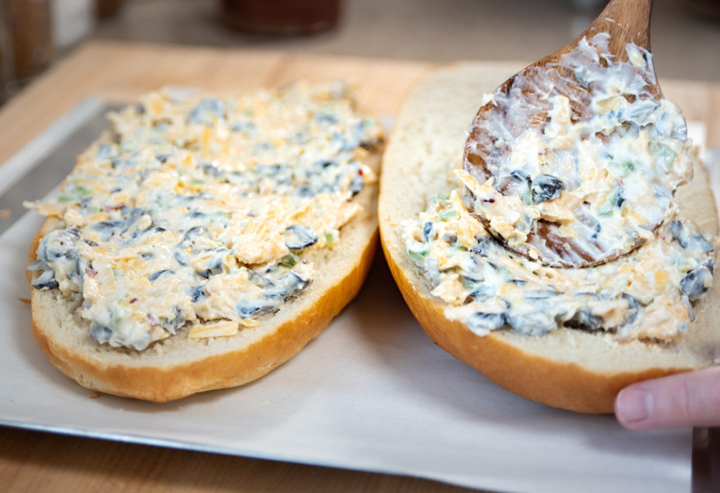 Spreading the cheesy topping evenly onto the French bread for Mexican Garlic Cheese Bread