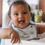 A baby sitting in a highchair, laughing