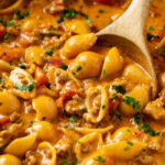 A wooden spoon scooping up taco pasta from a pot.