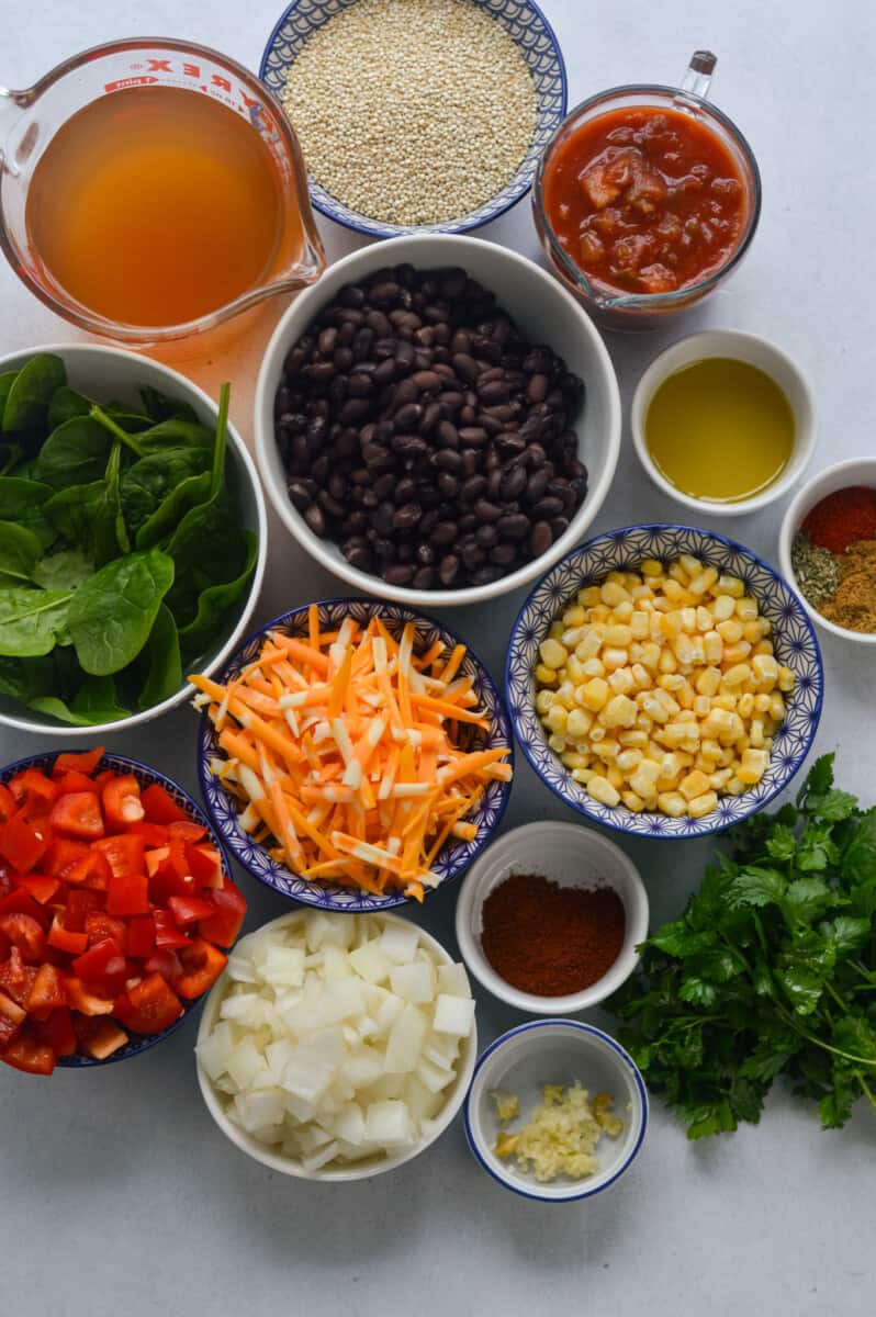 Ingredient lay flat featuring quinoa, black beans, cheese, corn, spices, onion, red bell pepper, cilantro, broth, salsa, and spinach, ready to be used in the taco skillet recipe.