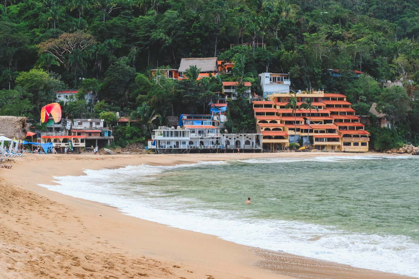 A lone swimmer enjoying the tranquil ocean at Yelapa Beach in the morning, with hotels visible in the distance.