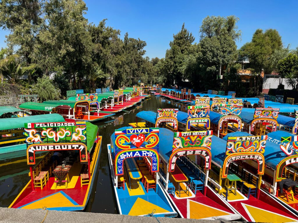 Colorful trajineras boats navigating the canals of Xochimilco, with festive decorations and passengers.