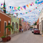 A street in Valladolid painted in bright colors, with multicolored triangular flags hanging between the buildings.