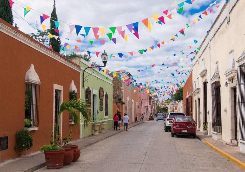 A street in Valladolid painted in bright colors, with multicolored triangular flags hanging between the buildings.