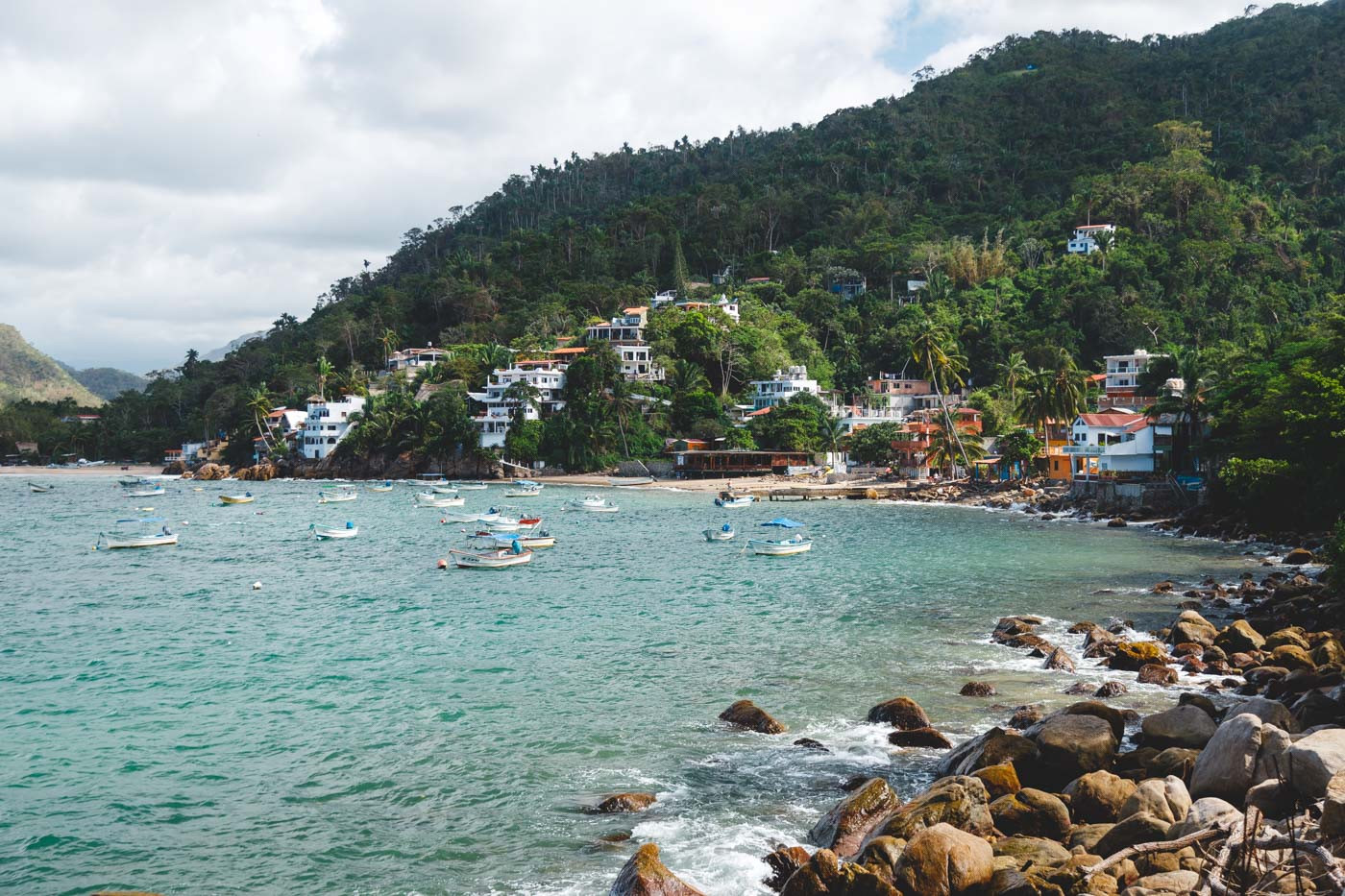 A picturesque view of small boats anchored in a Yelapa bay with beach villas nestled into the forested mountainside.