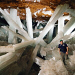 Photgraph shows a person in the Cave of Crystals with giant white gypsum crystals criss-crossing behind him.