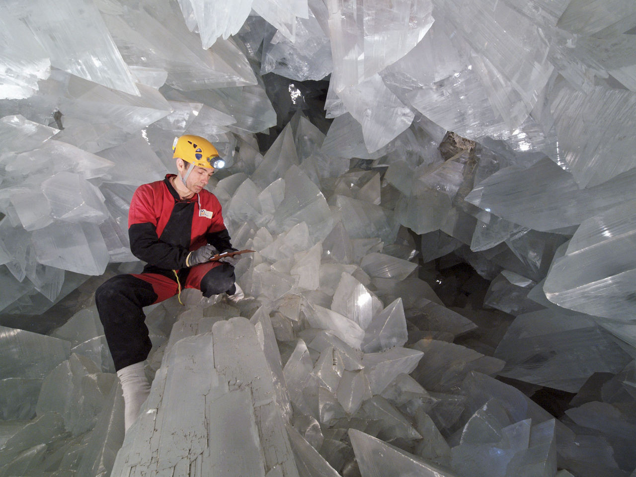 Photo shows a person inside a cave containing large, clear gypsum crystals.