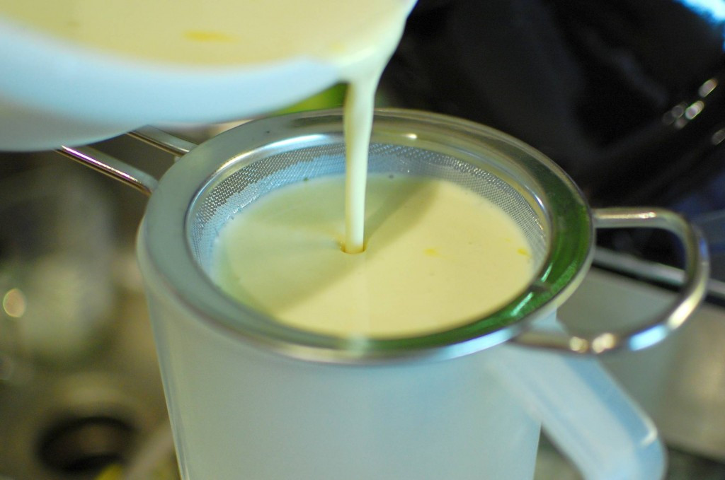 Custard mixture being strained through a sieve.