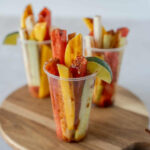 Sliced fruit in cups on a circle wooden board.