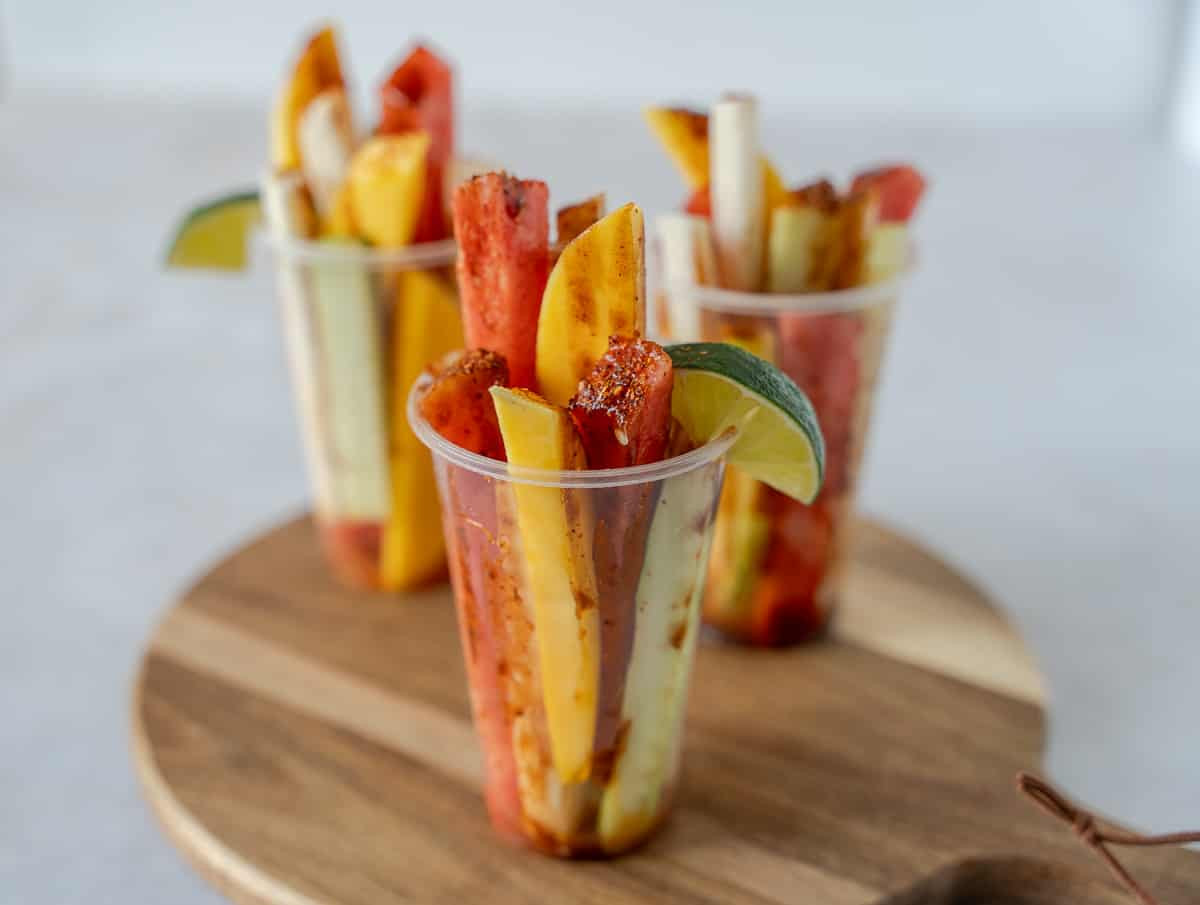 Sliced fruit in cups on a circle wooden board.