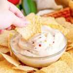 Hand holding a tortilla chip dipping into white sauce