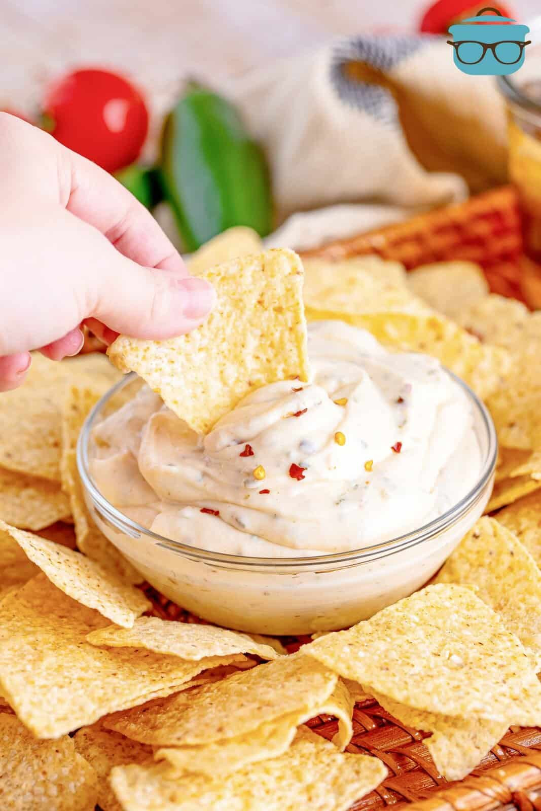 Hand holding a tortilla chip dipping into white sauce