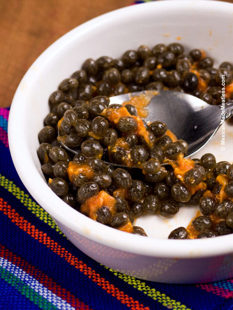 Black papaya seeds inside a small white bowl.