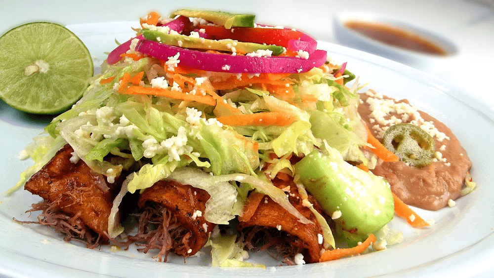 Enchiladas, corn tortillas dipped in a sauce, filled with cheese, meat or vegetables, rolled up and baked or fried, topped with sauce, cheese, sour cream, onions and cilantro
