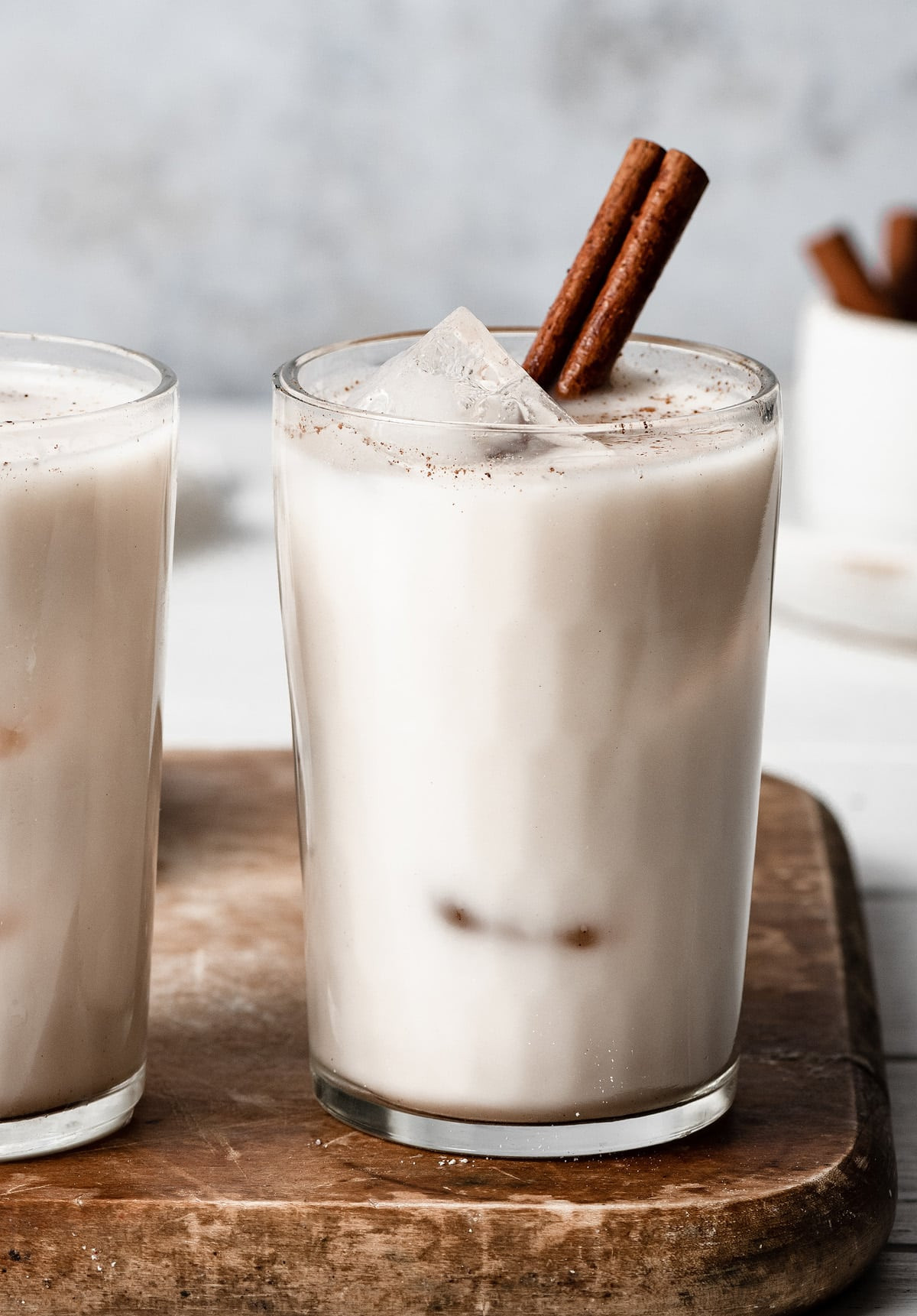 Close up image of horchata in a glass cup with ice cubes and garnished with a cinnamon stick.