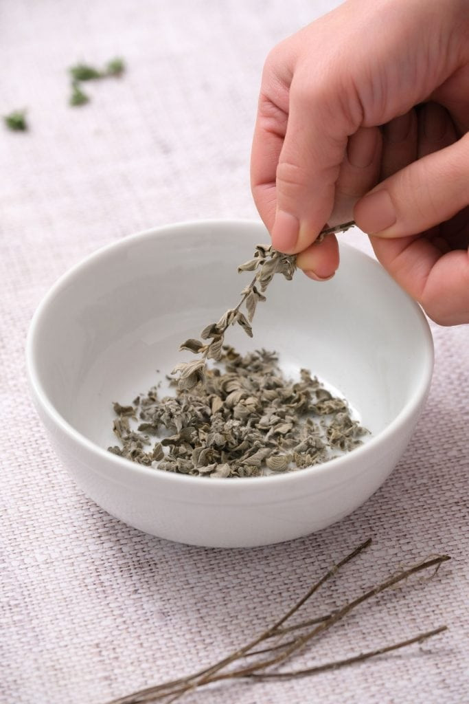 Hand crumbling oregano into white bowl