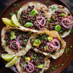 Overhead view of black bean tacos and lime wedges on brown plate.