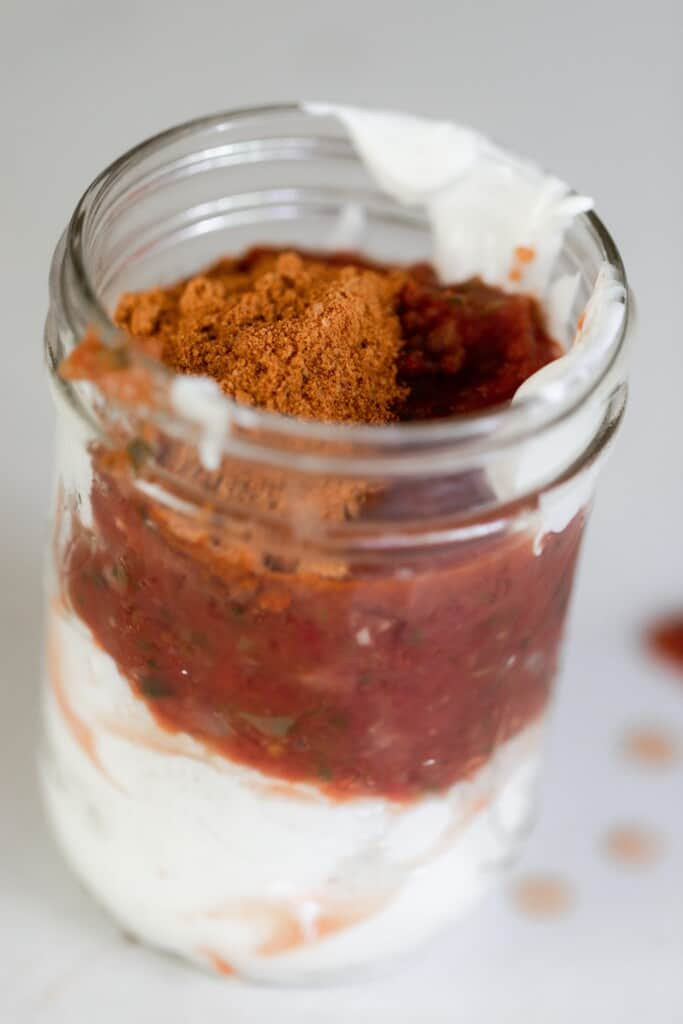 Mason jar with sour cream, salsa, and taco seasoning layers for Mexican ranch.