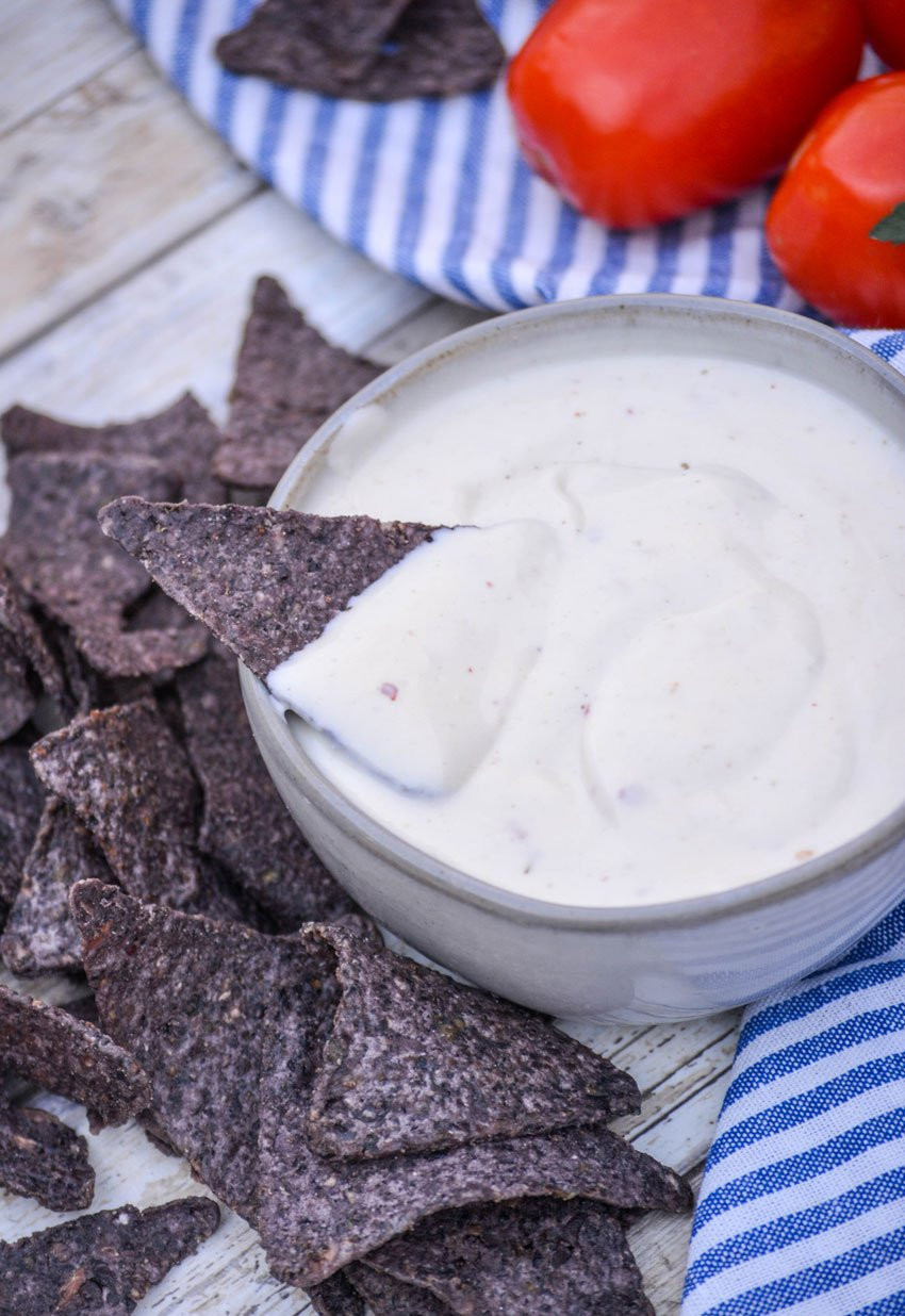 A blue corn chip dipped in a gray bowl filled with Mexican white sauce