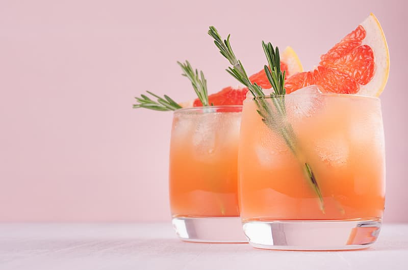 A refreshing Paloma cocktail in a tall glass with a lime wedge, set against a bright, sunny background, emphasizing its refreshing and thirst-quenching qualities.