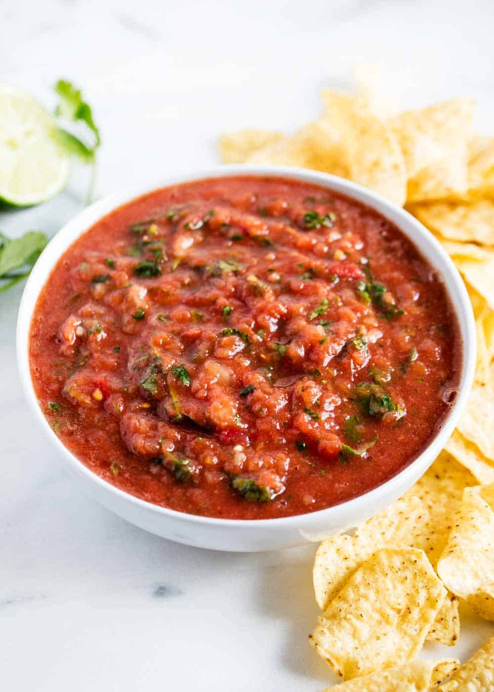 A bowl of homemade restaurant-style salsa served with crispy tortilla chips, garnished with fresh cilantro, sitting on a rustic wooden table