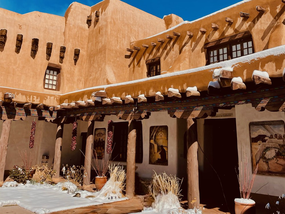Traditional adobe style building with a courtyard filled with snow in Santa Fe, New Mexico.