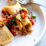 Close-up of a steamy, freshly unwrapped tamale revealing its savory filling.