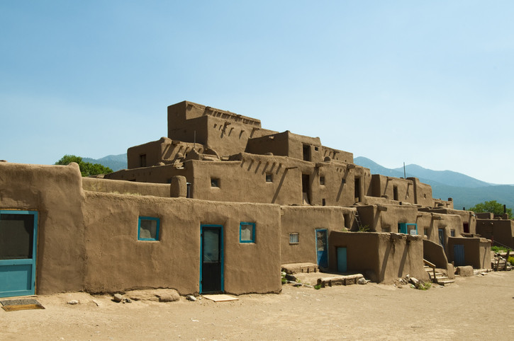 Adobe-style buildings with blue doors, set against a clear sky and mountains in the background.