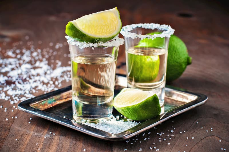 Close-up of a tequila bottle and glasses with a blurred background of a Mexican bar, showcasing the details of the tequila and its presentation.