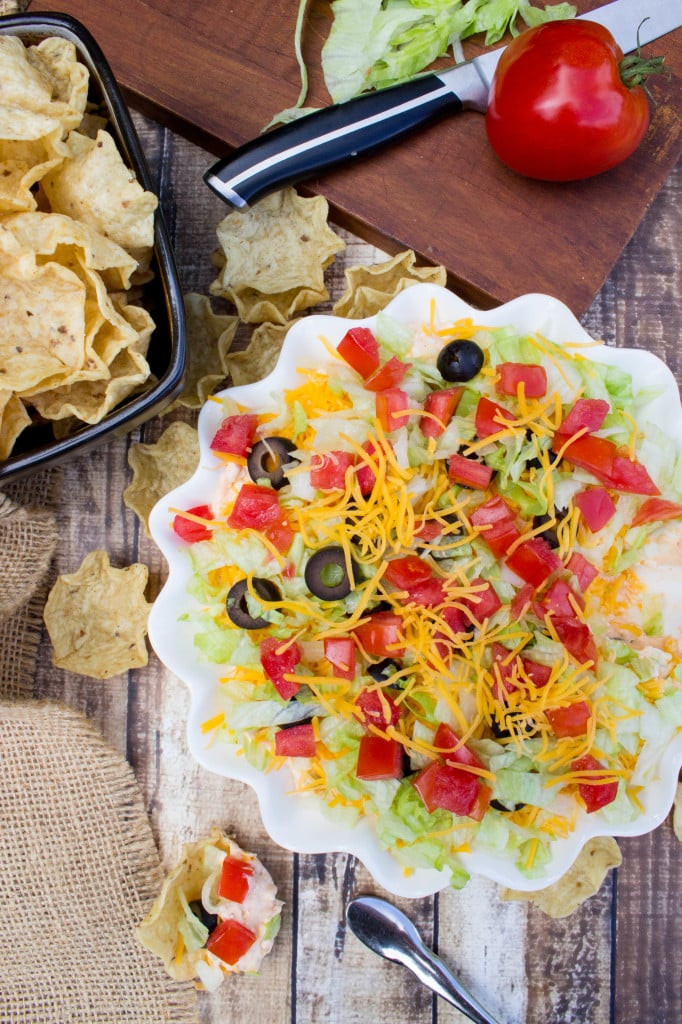 Overhead view of a taco dip with various toppings in a white serving dish.