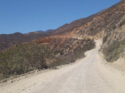 The dirt road to Puerto Santo Tomas winds through farmlands and steep mountainsides, requiring caution and a suitable vehicle.