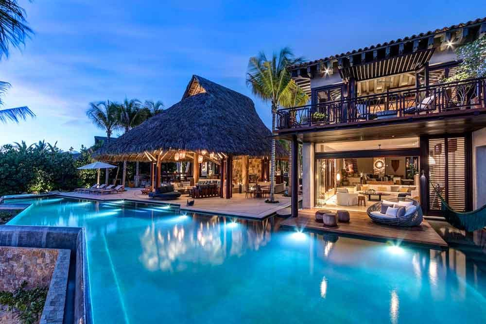 An aerial view of a luxury house located next to a beautiful tropical beach