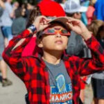 A child using solar eclipse glasses to safely view the solar eclipse.