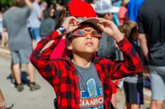 A child using solar eclipse glasses to safely view the solar eclipse.